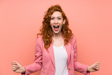 Redhead woman in suit over isolated pink wall with surprise facial expression