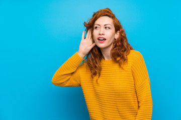 Redhead woman with yellow sweater listening to something by putting hand on the ear