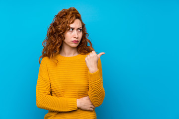 Redhead woman with yellow sweater unhappy and pointing to the side