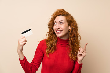 Naklejka premium Redhead woman with turtleneck sweater holding a credit card