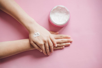 Female hands with cream on a pink background in minimal style. Skin care, beauty and health.