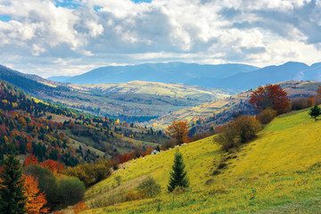 Fototapeta na wymiar autumn landscape. village on the hillside. forest on the mountain covered with red and yellow leaves. over the mountains the beam of light falls on a clearing at the top of the hill.