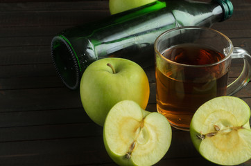 A glass of Apple cider vinegar with green apples and the laying bottle of cider on wooden background, space for text