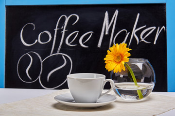 Cup of coffee and bowl of gerberas on a background of graphite Board with the inscription 