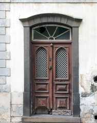 an old ornate brown double house door with broken repaired panels and hand shaped knocker with...