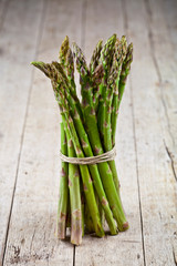 Bunch of fresh raw garden asparagus on rustic wooden table background. Green spring vegetables.