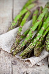 Bunch of fresh raw garden asparagus closeup and linen napkin on rustic wooden table background. Green spring vegetables.