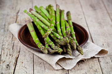 Fresh raw garden asparagus closeup on brown ceramic plate and linen napkin on rustic wooden table background. Green spring vegetables.