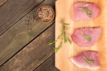 Pork steaks with spices and greens on wooden background