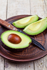 Fresh organic avocado on ceramic plate and knife on rustic wooden table background.