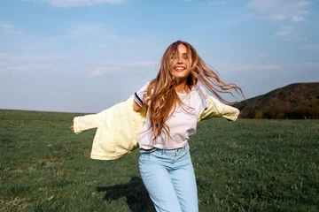 Outdoors lifestyle fashion portrait of happy smilling blonde girl. Beautiful smile. Long curly light hair. Wearing stylish yellow jacket and jeans. Joyful and cheerful woman. Happiness © svitlychnaja
