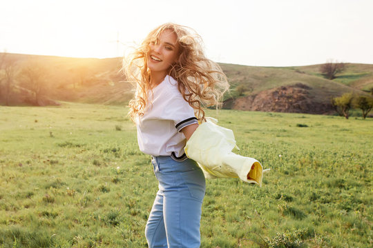 Outdoors lifestyle fashion portrait of happy smilling blonde girl. Beautiful smile. Long curly light hair. Wearing stylish yellow jacket and jeans. Joyful and cheerful woman. Happiness