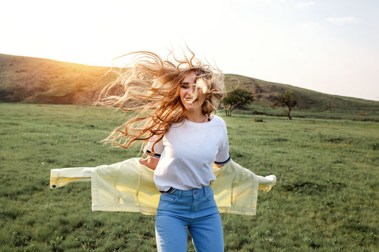 Outdoors lifestyle fashion portrait of happy smilling blonde girl. Beautiful smile. Long curly light hair. Wearing stylish yellow jacket and jeans. Joyful and cheerful woman. Happiness