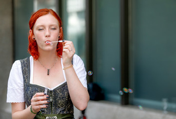 Young pretty redhead ginger girl making rainbow bubbles wearing a dirndl at a wedding feeling happy