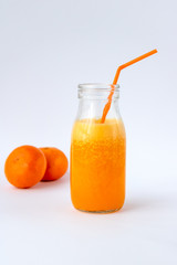 Tangerine smoothie in a glass bottle on a white background. In the background the tangerines are blurred.