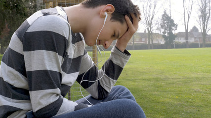 tired teen boy with smart phone listening or talking while sitting in british park. teenager and...