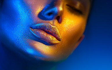 Fashion model woman face in bright sparkles, colorful neon lights, beautiful sexy girl lips. Trendy glowing gold skin make-up. Glitter metallic shine makeup