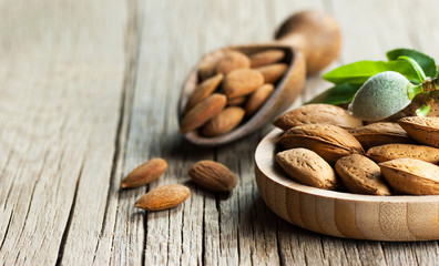 Almond nuts in wooden shovel, almonds with shell in bamboo bowl on wooden background with green...