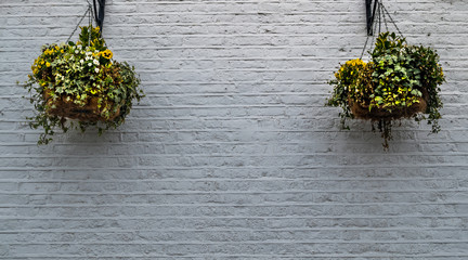 2 flower pots hanging on a white brick wall outside the house.