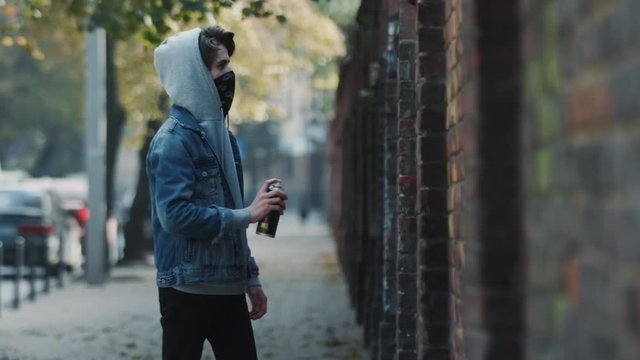 Young male artist drawing a street art graffiti with aerosol spray bottle on the wall in the modern city
