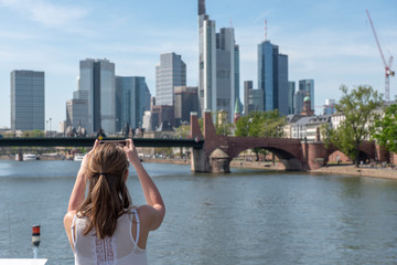 Fototapeta na wymiar Eine junge Frau beim Fotografieren der Skyline von Frankfurt am Main
