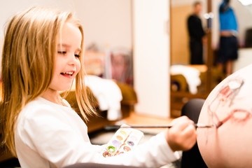 Little blonde girl painting little baby brother or sister on her mothers pregnant belly with water colors and paint brush