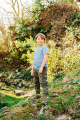Cute little boy playing in summer park, green nature background, wearing blue t-shirt and khaki trousers