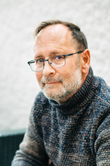 Outdoor portrait of 50 year old man wearing brown pullover and eyeglasses