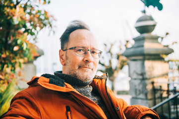 Outdoor portrait of middle age man wearing eyeglasses and orange winter jacket