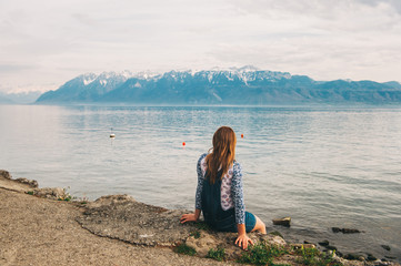 Young kid girl sitting by the lake on swiss side admiring French Alps