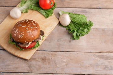 big burger with fried mushrooms and cheese above salad leaves, wooden table 