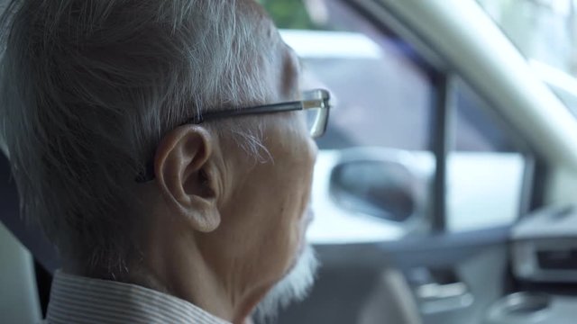 Back view of elderly man with gray hair sitting inside a car. Shot in 4k resolution
