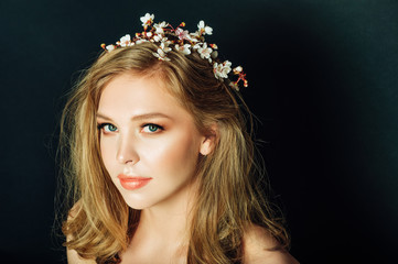 Close up portrait of beautiful young woman with blond hair and professional make up, posing on black background, wearing spring blooming branch of peach flowers