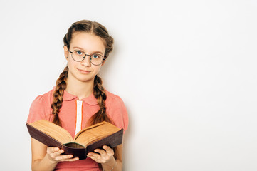 Studio portrait of cute preteen girl with two braids, holding heavy book, wearing glasses