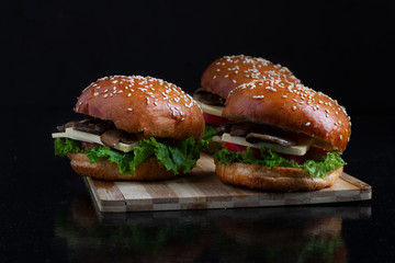 three mushrooms burgers together on kitchen board, dark background and law key