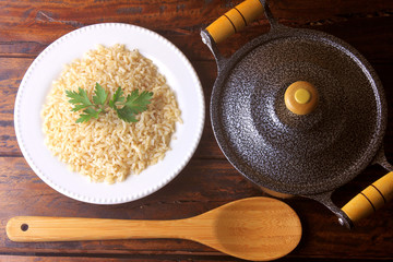 brown rice cooked in the dish next to pot and bamboo spoon in the kitchen on rustic wooden table