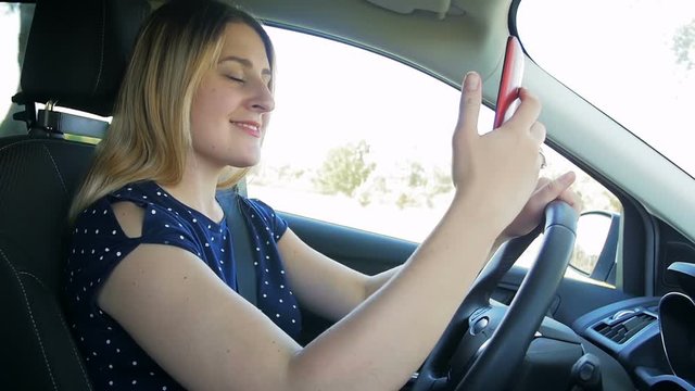 Slow motion video of young woman making selfie photo of smartphone while driving a car. Please be responsible and don't use gadget or electronic devices while driving vehicle