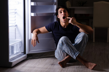 Fototapeta premium Man breaking diet at night near fridge