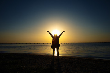 A girls a figure in the sunset by the sea. last rays of the Sun on the surface of the sea. A girl putting hands in the air.