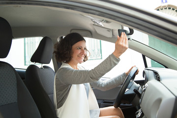 Cheerful female car driver looking in mirror. Positive young woman adjusting rearview mirror. Rearview concept