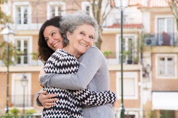 Joyful mother and daughter saying goodbye to each other. Young and senior woman smiling and hugging. Hug concept