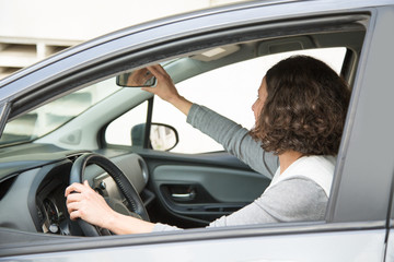 Side view of woman ready to drive. Young female car driver adjusting back mirror. Commuter concept