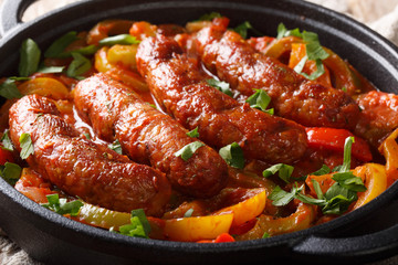 Traditional grilled sausages with multicolored peppers, onions and tomatoes close-up in a pan. horizontal