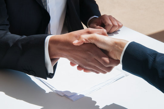 Closeup of business people shaking hands outdoors. Business man and woman wearing formal clothes and sitting at table with papers. Agreement concept.