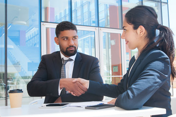 Serious business people shaking hands in outdoor cafe. Business man and woman wearing formal clothes and sitting with building glass wall in background. Deal concept.