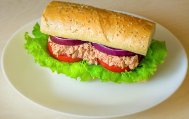 Tuna sandwich on wooden table. Selective focus. White plate. Tuna, lettuce, onion, tomato, bread. Sandwich with fish and vegetables.