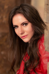 Naklejka premium Fashion portrait of a gorgeous young woman in red leather jacket, sitting in a door of an old abandoned building, looking at the camera. Close-up shot, retouched for perfect skin, vibrant colors
