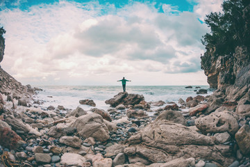The girl stands on a stone by the sea.