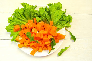 Sliced pumpkin slices on lettuce leaves with pine nuts and arugula. Olive oil, honey and Provencal herbs. Supply of salad in a white plate. Textured wooden table in a rustic style.