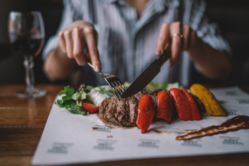 Spicy grilled lamb leg with vegetables and herbs on a roasting cast iron. Barbecue lamb with vegetables. Healthy food. Eating and leisure concept. Woman having dinner at table with food. Toned image.
